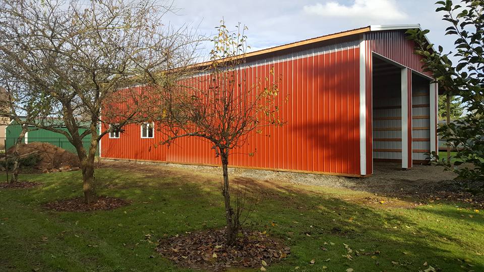 Picture of a large red pole barn with two overhead doors. Picture is taken from the side.