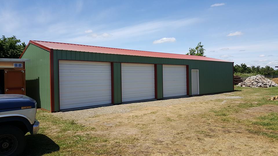 Picture of a green pole building with three overhead doors and one man door.