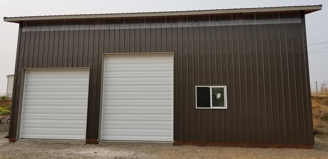 Picture of a large brown pole building with two different sized overhead doors closed.