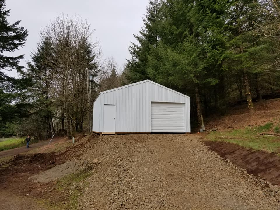 Picture of a white garage/workshop on top of a hill with one overhead door and a man door.