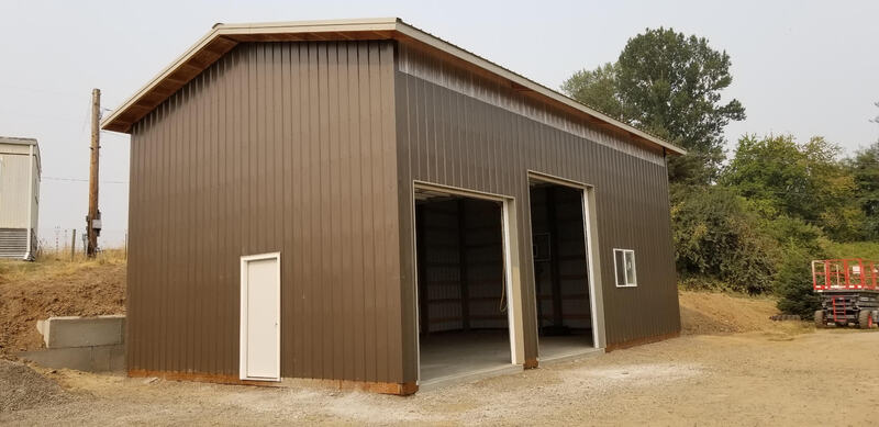 Picture of a tall brown pole building with two different sized overhead doors open.